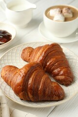 Plate with tasty croissants served on white wooden table, closeup