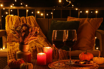 Glasses of wine, burning candles and autumn decor on outdoor terrace in evening - obrazy, fototapety, plakaty