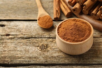 Bowl of cinnamon powder and sticks on wooden table. Space for text