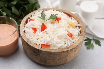 Bowl of delicious rice with vegetables and parsley on light table, closeup