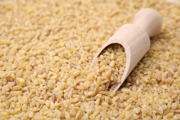 Wooden scoop and raw bulgur as background, closeup. Space for text