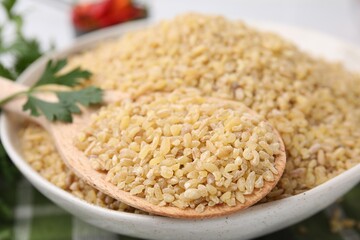 Bowl and spoon with raw bulgur on table, closeup