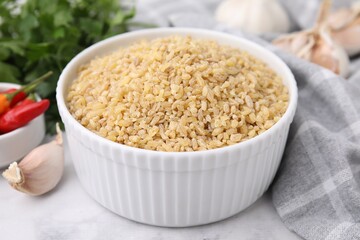 Raw bulgur in bowl and spices on table, closeup