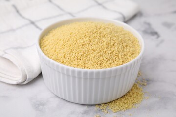 Raw couscous in bowl on light table, closeup