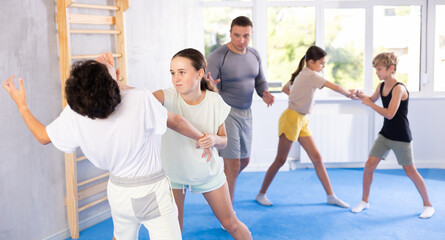 Fototapeta premium Girls and boys practicing in pair self-defence movements with female trainer supervision