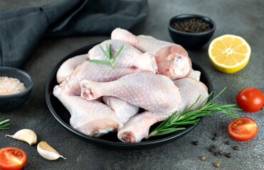 Uncooked chicken legs or drumsticks with rosemary, spices and vegetables.