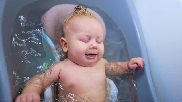 Lovely infant baby lies relaxed in the bath. Cute plump child waving hands and feet actively in water.