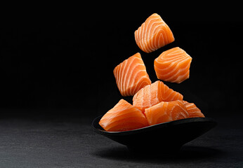 Falling salmon cubes isolated on black background with copy space