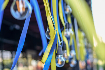 Flattering blue and yellow ribbons hanging with retro light bulbs string. Selective focus. Low DOF.