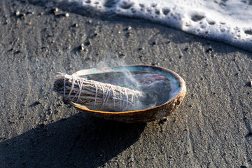An image of a burning sage smudge stick on a sandy beach with an incoming ocean wave.  