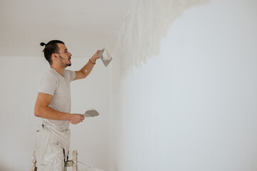 A builder is on ladder is skim coating and plastering walls.