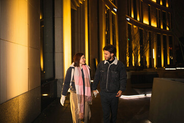 Fototapeta na wymiar loving couple in winter clothes walks the city in the evening, happy young people in cold weather.