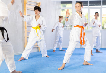 Group of preteen children in kimono trying new martial moves at karate class