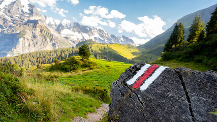 White and red trail waymark in a hiking path in the Swiss Alps with blurred background - trail...