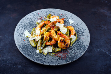 Traditional fried king prawns with Italian foglie di olivo pasta and parmesan cheese served as close-up on a design plate with text space