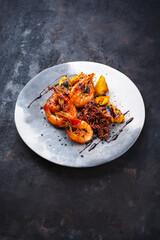 Traditional fried king prawns with pineapple pieces and brown rice served as close-up on a design bowl with text space