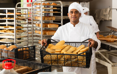 man in chefs uniform with bread in tray in bakery