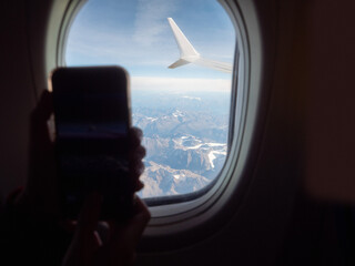 Fototapeta premium View from an airplane window of a mountain area and left wing, warm sunny day. Travel and tourism view. Flying to holiday destination point. Scene through illuminator. High viewpoint.
