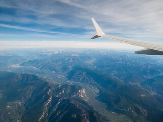 View from an airplane window of a mountain area and left wing, warm sunny day. Travel and tourism view. Flying to holiday destination point. Scene through illuminator. High viewpoint.