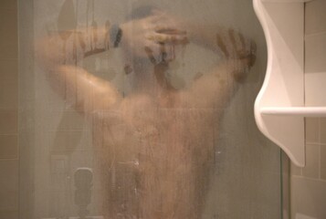 40-year-old man in the shower, back against the foggy screen with his arms behind his head.