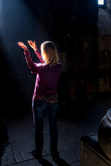 A woman in an ancient temple puts her hands up to the light pouring in from the window.