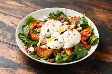 Roasted butternut squash salad served with poached eggs, spinach, nuts and pomegranate seeds