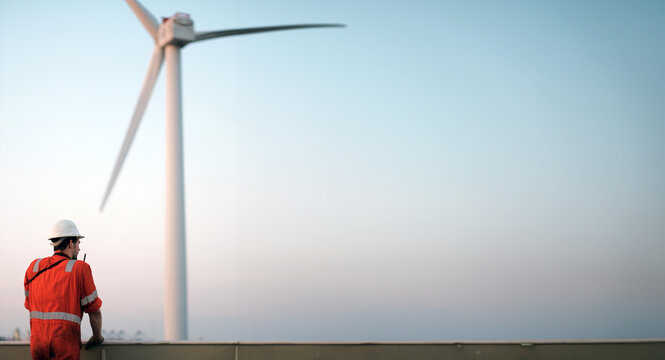 Offshore technician. Seafarer. Seaman. Navigator. A Man in a Boiler Suit is Standing In Front Of The Wind Generator. Seafarer In front of the Wind Generator. Wind Farm Construction Site.