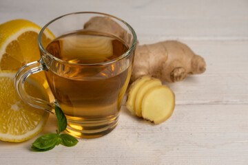 Cup of hot ginger tea with ginger root and lemon on gray background.