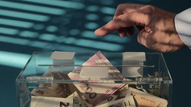 Hand give Charity in nominal 200 Ukrainian hryvnia UAH banknotes to a transparent donation box for money donation. A financial support, collects money for a noble cause. The act of giving supports 