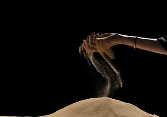 Hand releasing dropping sand on hill. Fine Sand flowing pouring through fingers hand against black...
