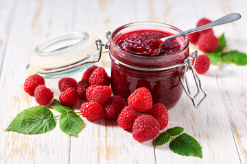 Spoon with delicious raspberry  marmalade or jam over jar on table. Space for text.