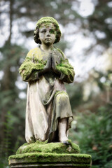 Fototapeta na wymiar Small moss-covered cherub kneeling in prayer on the base of a gravestone