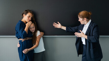 The teacher screams at the schoolgirl and her mother standing at the blackboard. 