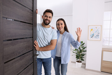 Happy couple waving near door. Invitation to come indoors