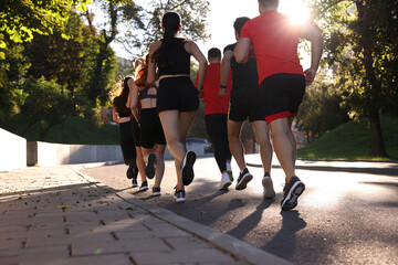 Group of people running outdoors on sunny day, back view