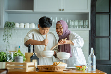 Cute son And His Muslim Mom In Hijab Preparing Pastry For Cookies In Kitchen, Baking Together At Home. Islamic Lady With son Enjoying Doing Homemade Pastry, preparing to cook breakfast for her family.