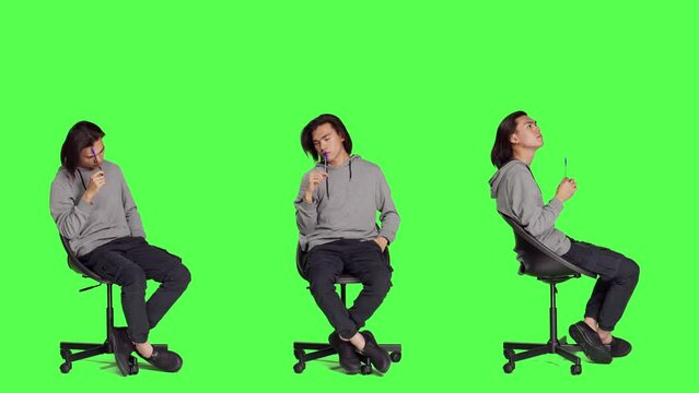 Person thinking about new solution over greenscreen backdrop, feeling doubtful and trying to solve dilemma. Asian guy sitting on chair and acting uncertain, pensive confused adult.