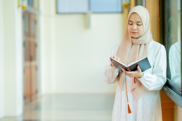 The image of an Asian Muslim woman in the Islamic religion in hijab in cream color. reading the...
