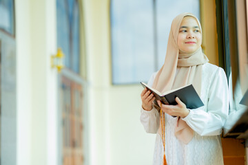 The image of an Asian Muslim woman in the Islamic religion in hijab in cream color. reading the...
