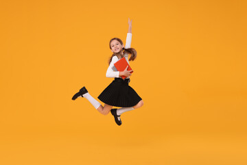 Happy schoolgirl with books jumping on orange background