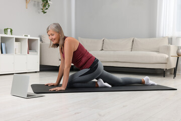 Senior woman in sportswear stretching while watching online tutorial at home