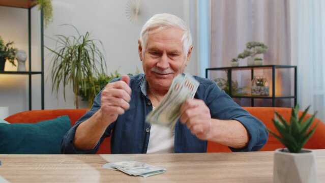 Planning family budget. Happy senior man counting money cash calculate domestic bills at home. Elderly old grandfather satisfied of income salary pension and saves money for planned vacation gifts