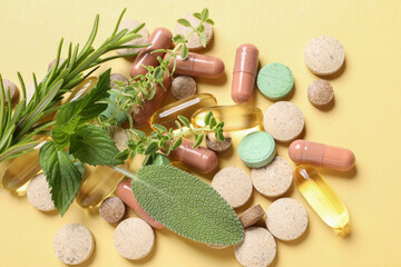 Different pills and herbs on light yellow background, flat lay. Dietary supplements