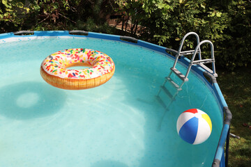 Inflatable ring and ball floating on water in above ground swimming pool outdoors