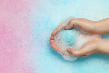 Woman holding bath bomb over water with foam, top view. Space for text