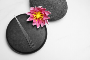 Acupuncture needles, spa stones and flower on white table, flat lay. Space for text