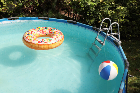 Inflatable ring and ball floating on water in above ground swimming pool outdoors