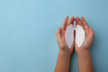Child holding paper human lungs on light blue background, top view. Space for text