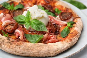 Delicious pizza with burrata cheese, basil, ham and sun-dried tomatoes on plate, closeup