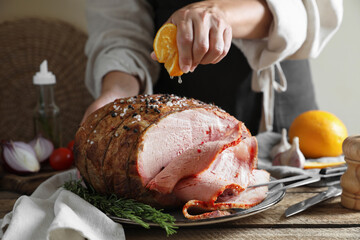 Woman squeezing juice from orange slice onto delicious baked ham at wooden table, closeup